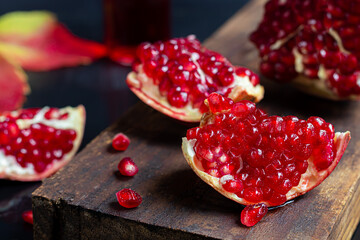 Large pomegranate, broken into pieces. On a dark background. Grains are scattered nearby. Autumn concept. Vitamins, healthy lifestyle.