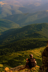 Naklejka premium A tourist sits on a rock and looks into the distance, photos on top of Mount Pip Ivan Chornohirsky, landscapes and epic photos of tourists in the mountains.