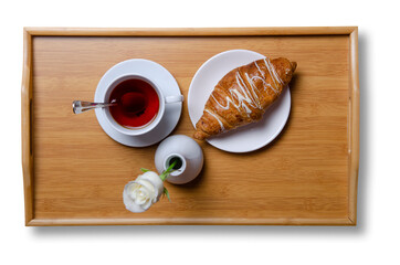 Cup of black tea and croissant, vase with white rose on wooden tray on white background isolation, top view