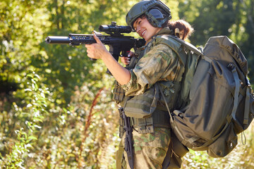 sportive caucasian woman soldier shooting with rifle machine gun in the forest, young slim female is hunting