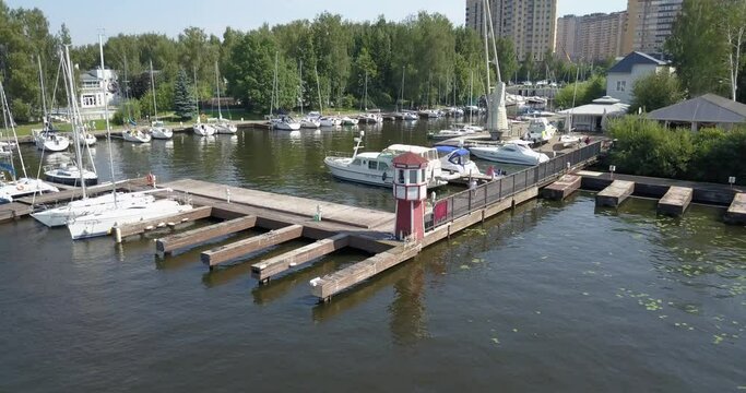 4K high quality calm windless bright summer morning aerial video of Moscow Channel yacht club embankment with wooden lighthouse, green trees, wooden pier, moored anchored boats near Moscow, Russia