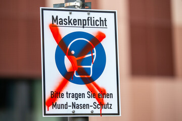 Info sign in a german city with german text. A riot marks it with a red x. Maskenpflicht, Bitte tragen Sie einen Mund-Nasen-Schutz. Mask compulsory, please wear mouth and nose protection.