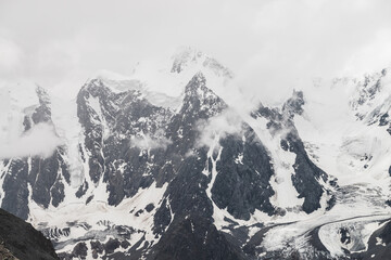 Atmospheric alpine landscape with massive hanging glacier on giant mountain. Big glacier tongue on mountainside. Low clouds among snowbound mountains. Cracks on ice. Majestic scenery on high altitude.