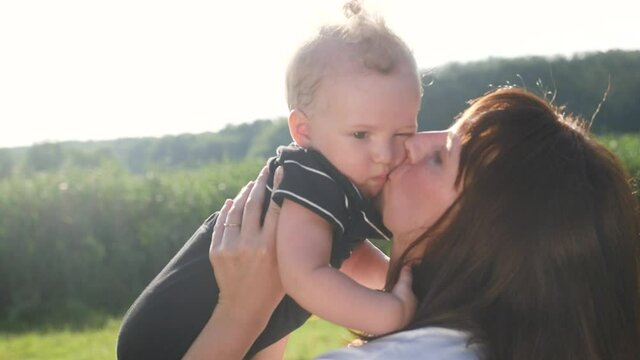 mom kiss newborn baby son holds in his arms playing in the park. mother day kid dream childhood happy family concept. parent play on hands with a little boy lifestyle son sunlight. people in the park