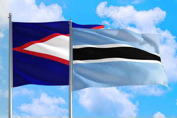 Botswana and American Samoa national flag waving in the windy deep blue sky. Diplomacy and...