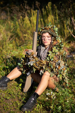 young and beautiful hunter woman have rest after successful hunting, sit on the grass in forest, wearing military wear and disguise