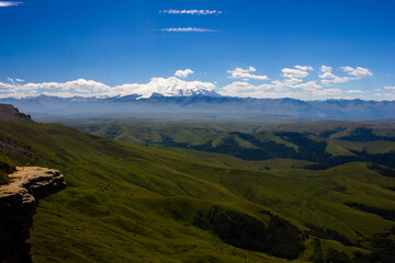 An excellent view from the plateau to the extinct volcano and the snowy peak of Mount Elbrus. Below is a green gorge
