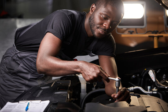 professional car mechanic is examining engine under the hood at auto repair shop, make notes, checking notes in notebook