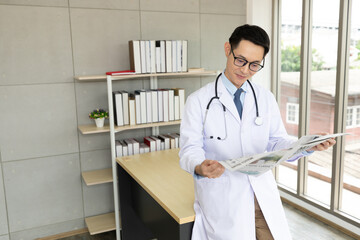 asian doctor reading a newspaper in medical office
