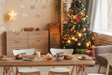 Background image of cozy home interior with Christmas tree and wooden table with snacks in foreground, copy space