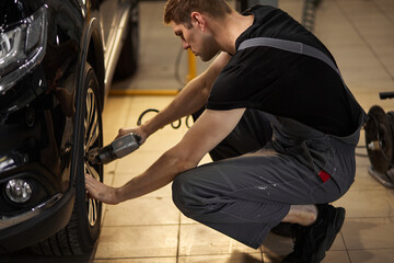 concentrated professional auto mechanic man repairs a wheel that has broken, changing