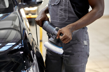 hardworking auto mechanic male is polishing car with the use of special equipment, apply it on car surface, repair and clean, renew