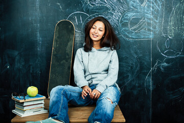 Fototapeta na wymiar young cute teenage girl in classroom at blackboard seating on table smiling, modern hipster concept