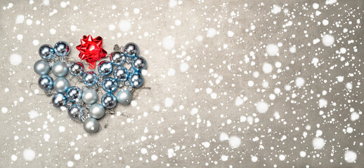 Christmas baubles in a gray and blue arranged in a heart shape on a winter background
