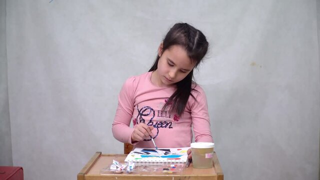 A cute girl draws a multicolored ornament on paper with acrylic paints and a brush.