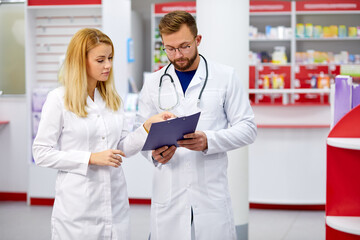 team of young caucasian chemists or druggists discussing medicines, check medical indications, in white medical gowns, at work place