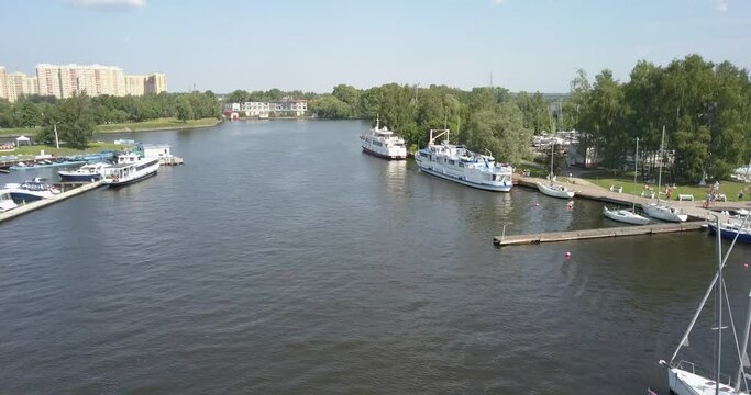 4K high quality calm windless bright summer morning aerial video of Moscow Channel yacht club embankment, green trees, wooden pier and shore with moored anchored boats and yachts near Moscow, Russia