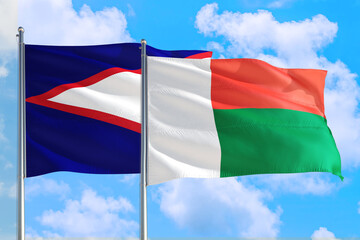 Fototapeta na wymiar Madagascar and American Samoa national flag waving in the windy deep blue sky. Diplomacy and international relations concept.