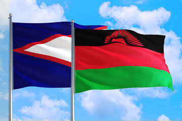 Malawi and American Samoa national flag waving in the windy deep blue sky. Diplomacy and...