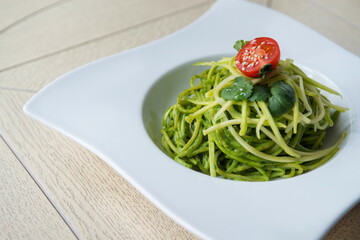 green spinach spaghetti with cheese and tomato on wooden table
