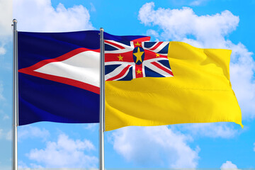 Niue and American Samoa national flag waving in the windy deep blue sky. Diplomacy and international relations concept.