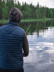 Pojke fiskar med fiskespö i hopp om att fånga en gädda eller abborre i en sjö i norra svenska vildmarken en fin sommarkväll.