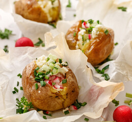 Oven baked potatoes stuffed with cand fresh vegetables sprinkled with chive close up view - obrazy, fototapety, plakaty