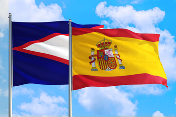 Spain and American Samoa national flag waving in the windy deep blue sky. Diplomacy and international relations concept.