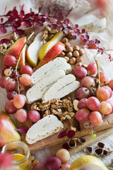 Sliced halloumi cheese with nuts, grapes and slices of pear on wooden board, selective focus.