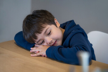 Obraz premium Portrait happy kid lying head down on his arm lookig out with smiling face, Day dream child laying head on table with little smile, Asianyoung boy sitting alone, Positive children