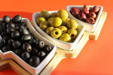 Green, black and red olives in a vase in the shape of a Christmas tree on a red background