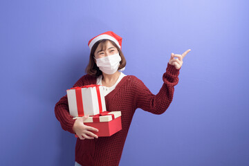 Portrait of young smiling woman in surgical mask wearing red Santa Claus hat isolated blue background studio.