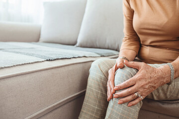 Senior woman holding the knee with pain. Old age, health problem and people concept - senior woman suffering from pain in leg at home. Elderly woman suffering from pain in knee at home