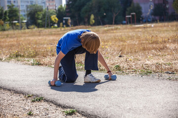 boy with dumbbells is engaged in fitness in the open air