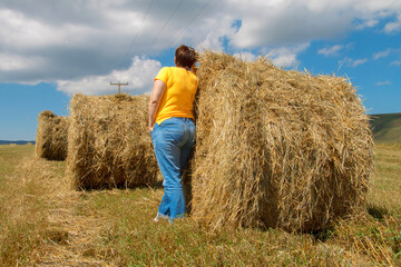 Naklejka na ściany i meble Woman near straw roll bales in harvested field at the daytime