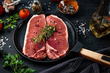  Raw beef steaks in a pan and spices for their preparation on a black background, close-up