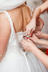 bridesmaid buttoning the dress on bride, details of beautiful lace wedding dress