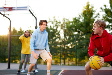 Fototapeta premium teens boys playing basketball on outdoor court, playground and having fun, caucasian young guys dribbling basketball with friends blocking