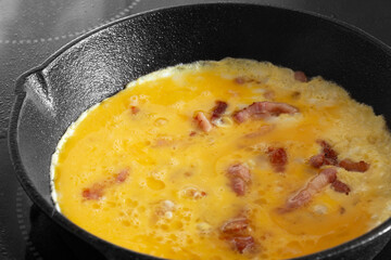 Omelette, with bacon, cooking on an electric hob or stove in a cast iron frying pan