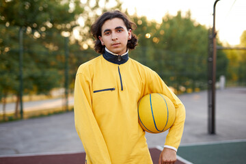 portrait of long haired caucasian teen boy with ball in ands, sportive boy keen on basketball