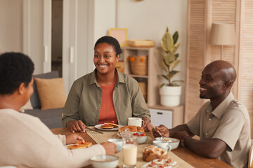 Portrait of smiling African-American woman sitting at dining table while enjoying breakfast with family at home