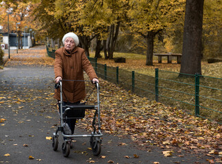 Elderly woman taking a walk in autumn with walker aid to enjoy fresh air