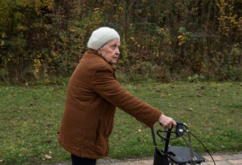 Elderly woman taking a walk in autumn with walker aid to enjoy fresh air