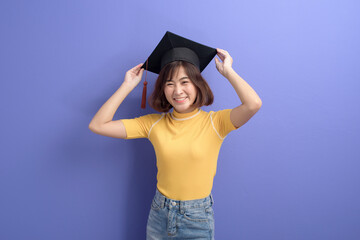 Portrait of young Asian student wearing graduation cap over studio background.