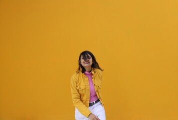 A very happy brown southeast Asian wearing yellow jacket and white pants laughing in front of a clear yellow wall 