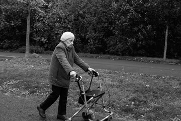 Elderly woman taking a walk in winter with the help of a walker aid in black and white