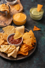 Appetizing corn tortilla chips on dark blue marble background. Salsa, cheese dip and avocado souse for taste. Unhealthy food. Traditional mexican dish.