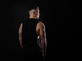 Fototapeta premium Handsome and fit bodybuilder posing on black background in workout gear