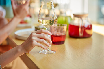 close-up photo of female hands holding glass of champagne in restaurant, table with beverages