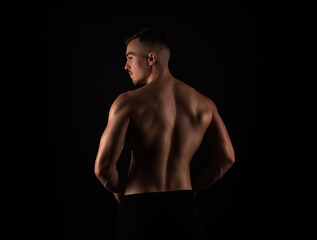 Fototapeta na wymiar Handsome young bodybuilder with muscular back standing on black background